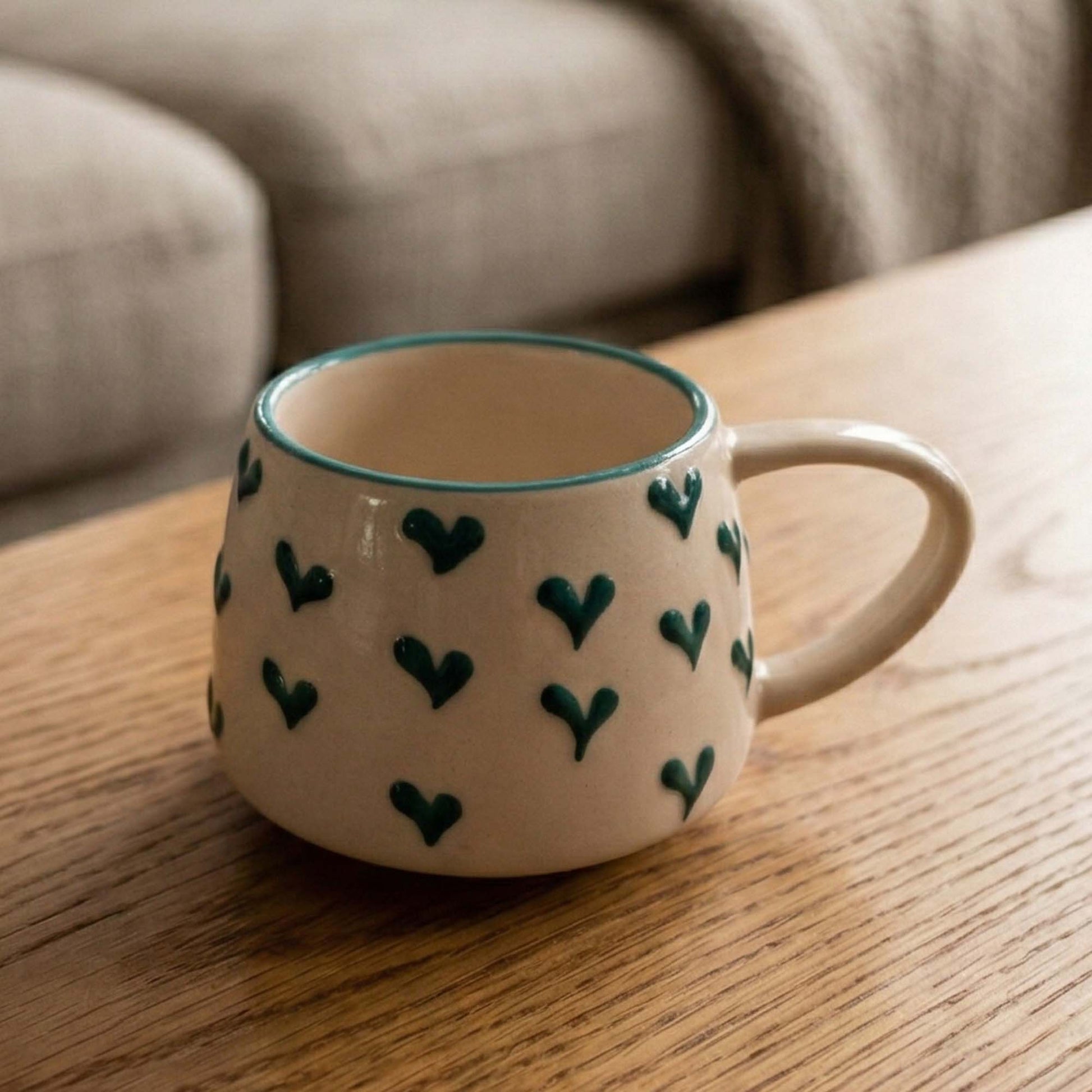 Ceramic mug with green heart patterns on a wooden surface