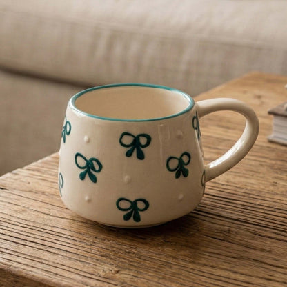 Ceramic mug with green bow designs on a wooden surface
