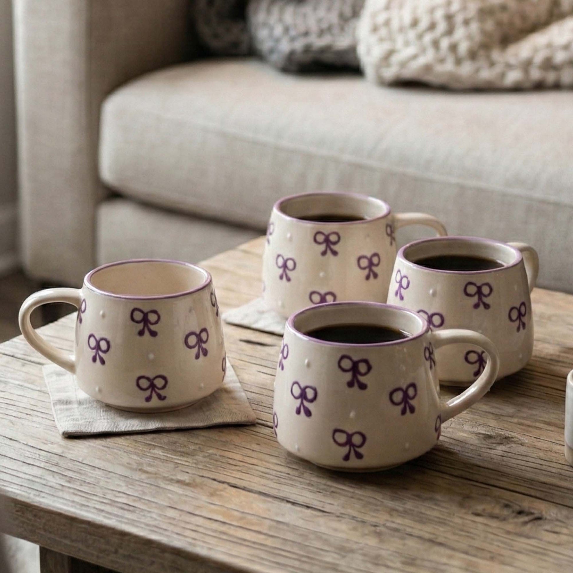 Four ceramic mugs with purple bow design on a wooden table.
