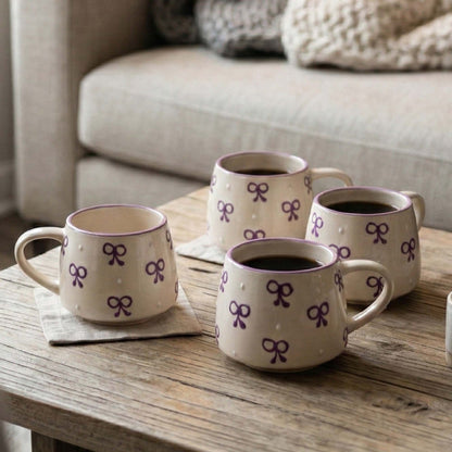 Four ceramic mugs with purple bow design on a wooden table.
