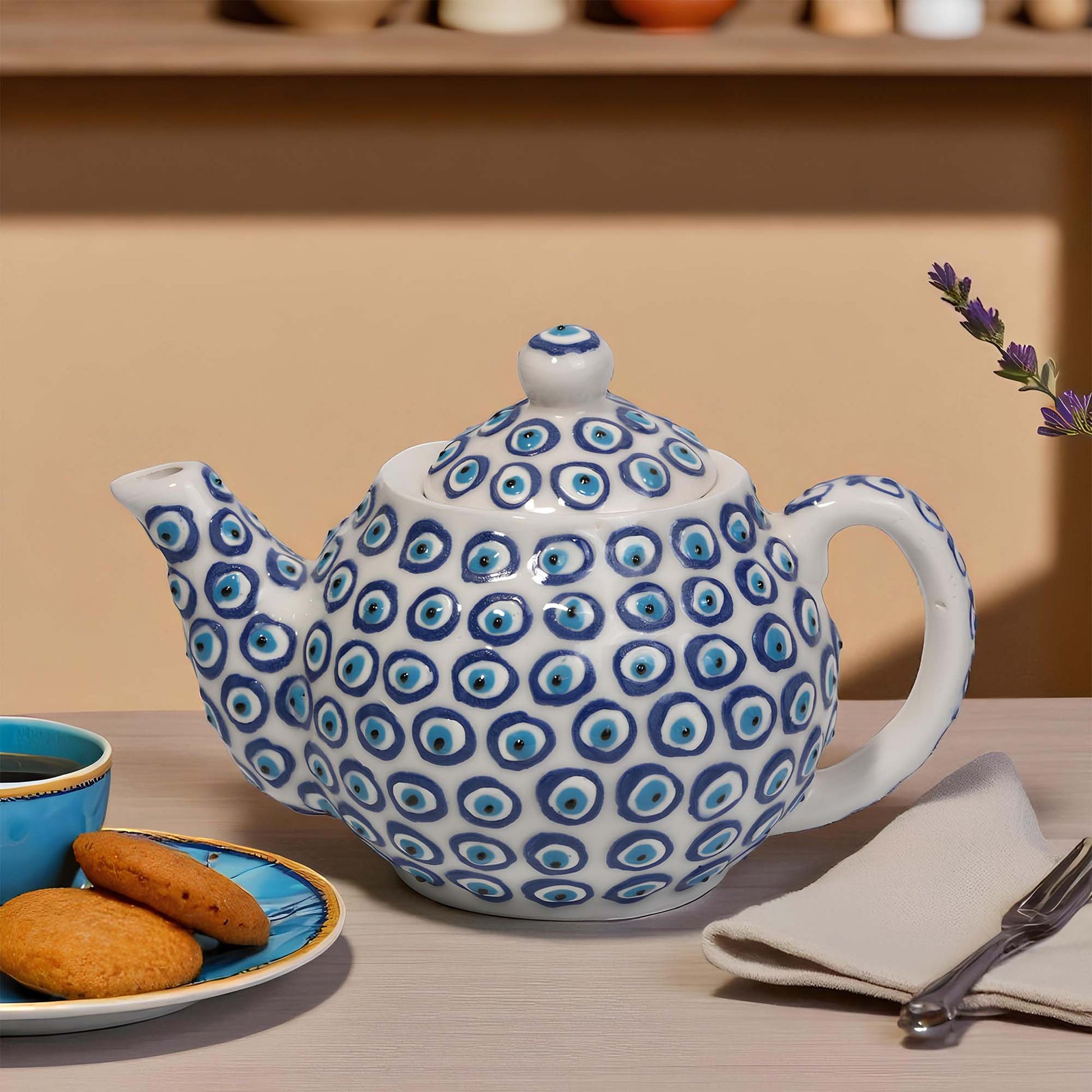 Ceramic teapot with blue circular pattern on a table with cookies and tea.