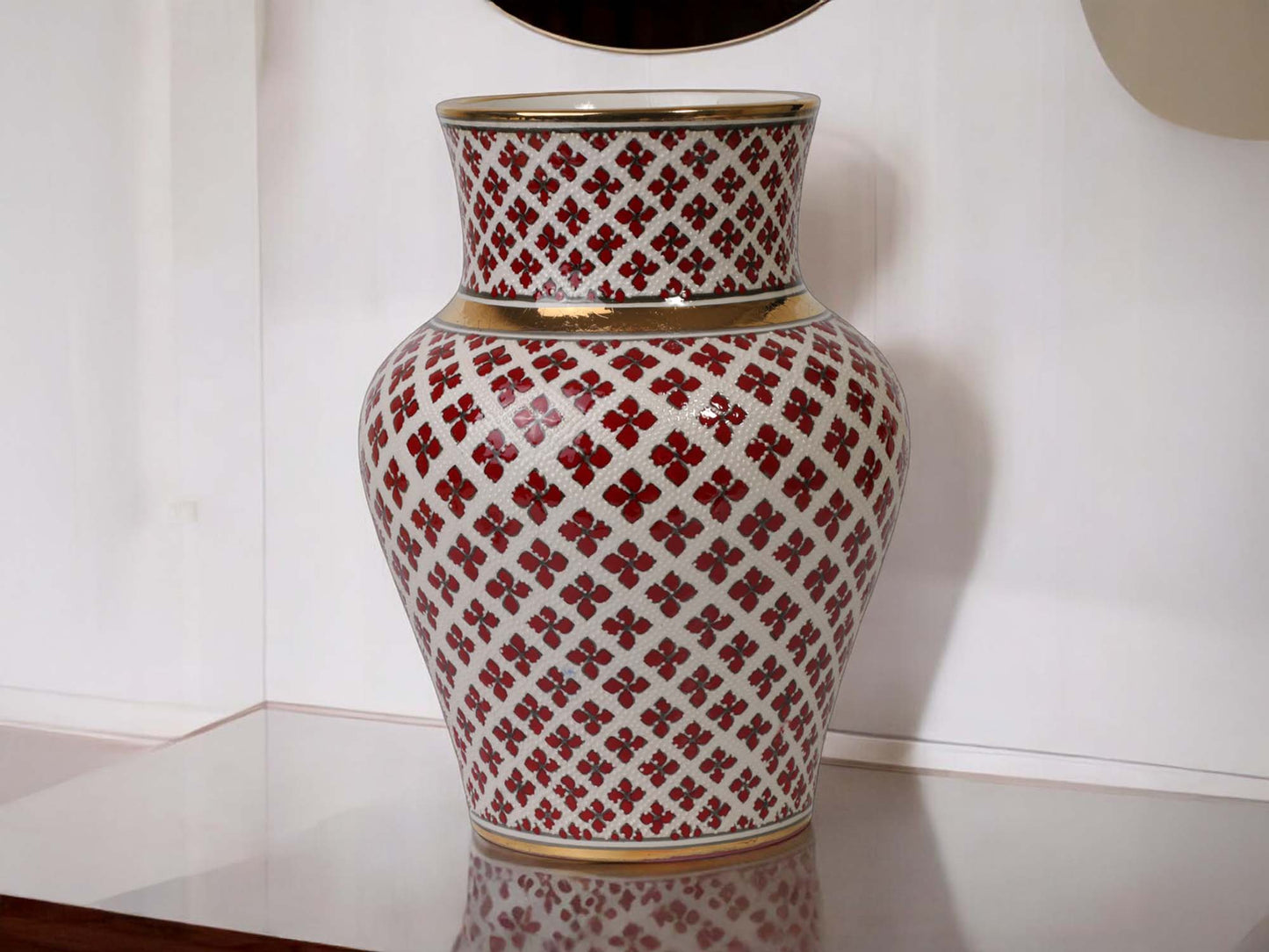 Decorative vase with red and white pattern on a reflective surface