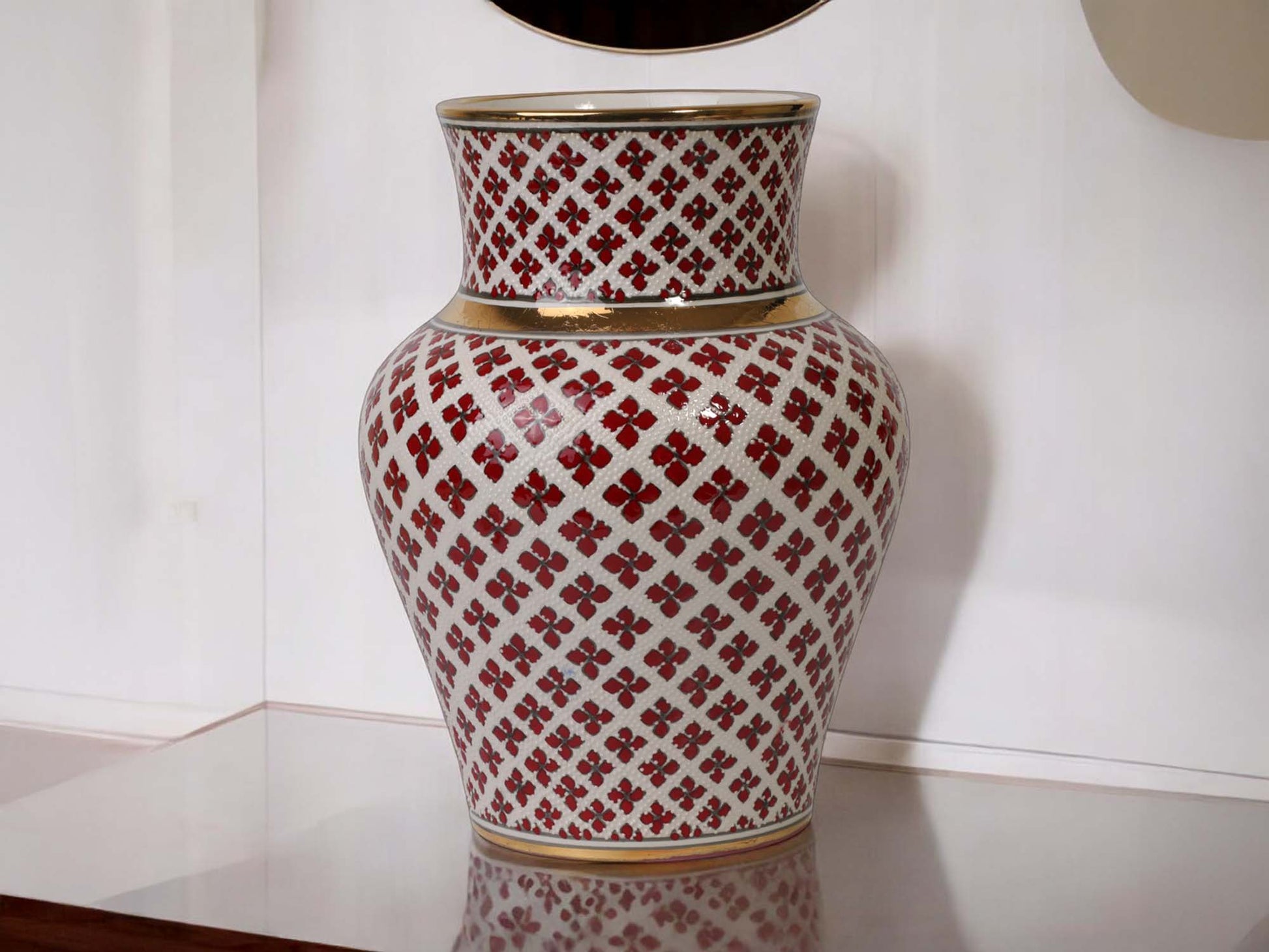 Decorative vase with red and white pattern on a reflective surface