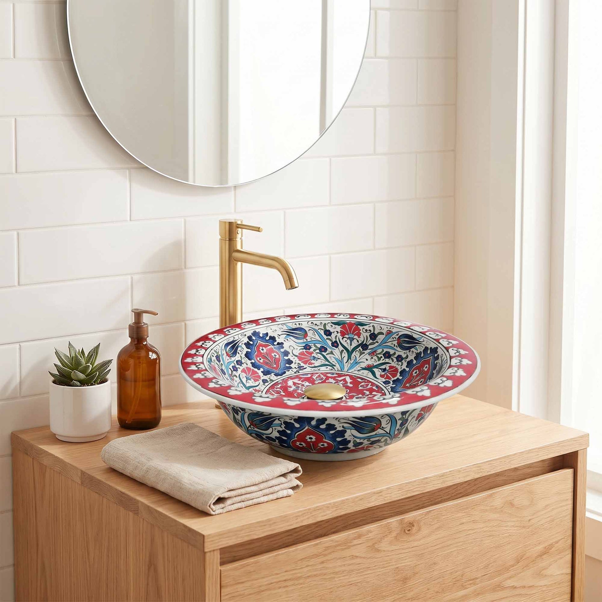 Bathroom vanity with a decorative floral sink, gold faucet, and small plant.