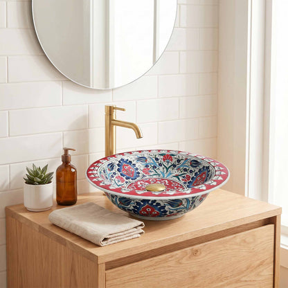 Bathroom vanity with a decorative floral sink, gold faucet, and small plant.