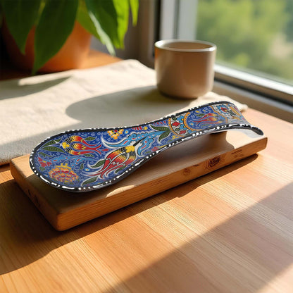 Colorful spoon rest on a wooden tray with a cup and plant in the background