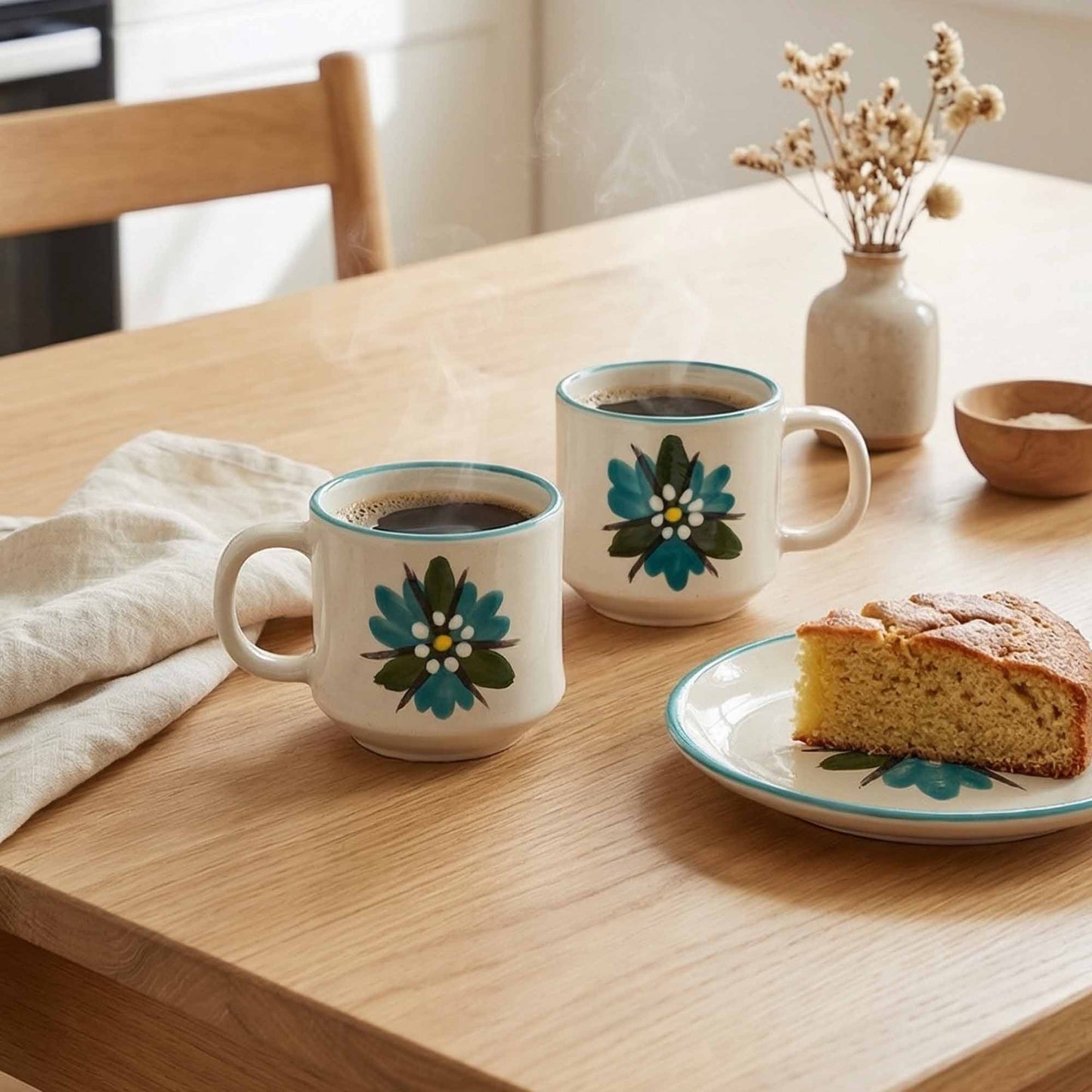 Two floral mugs with coffee and a slice of cake on a wooden table.