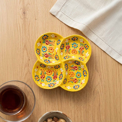 Yellow decorative snack platter with floral patterns on a wooden table with a glass of tea and a napkin.