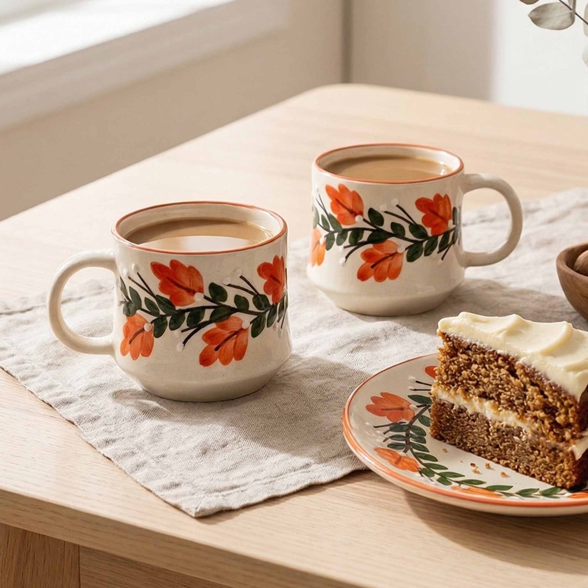Two floral-patterned mugs with coffee and a slice of cake on a wooden table.