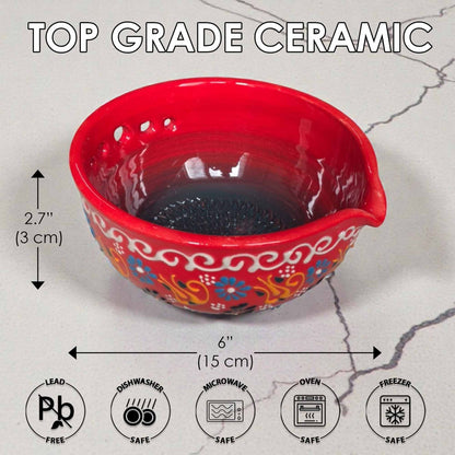 Red ceramic herb stripping bowl with floral patterns and measurements on a gray surface