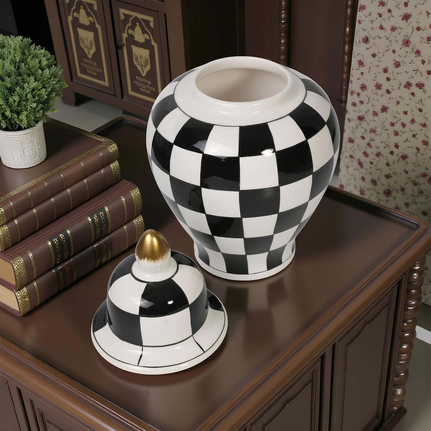 Black and white checkered vase on a wooden surface with books and a plant in the background.
