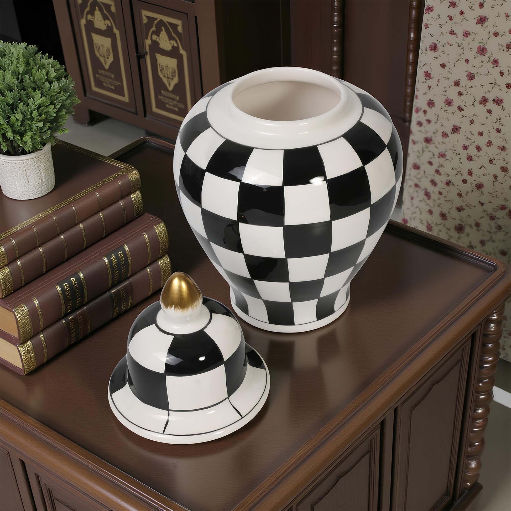 Black and white checkered vase on a wooden surface with books and a plant in the background.