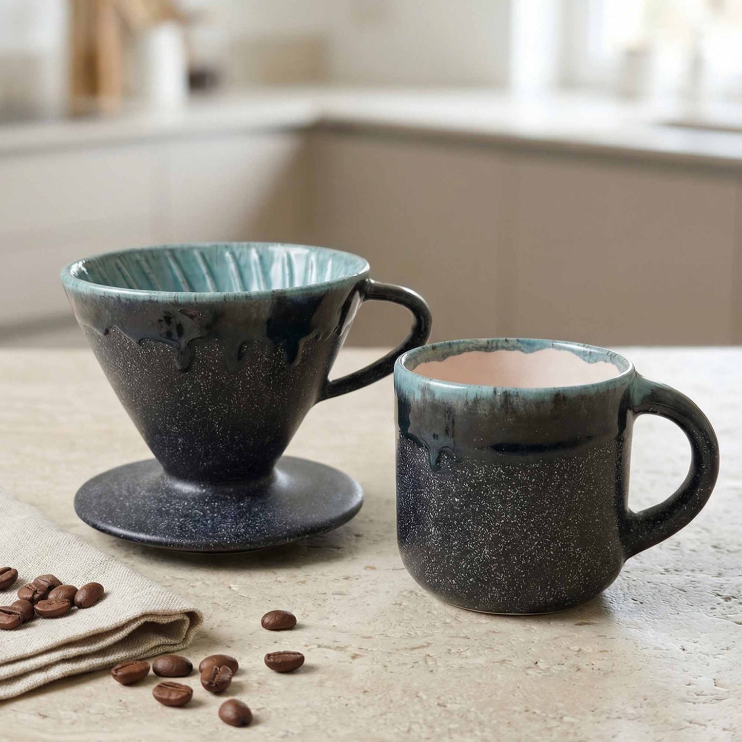 Two ceramic coffee cups on a table with coffee beans and a napkin.