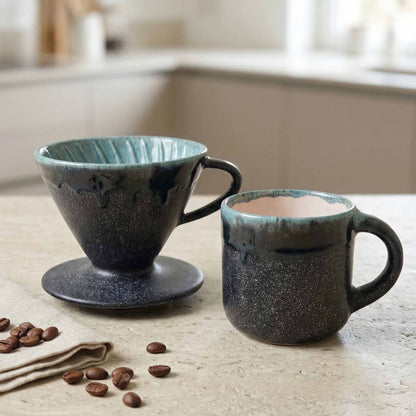 Two ceramic coffee cups on a table with coffee beans and a napkin.