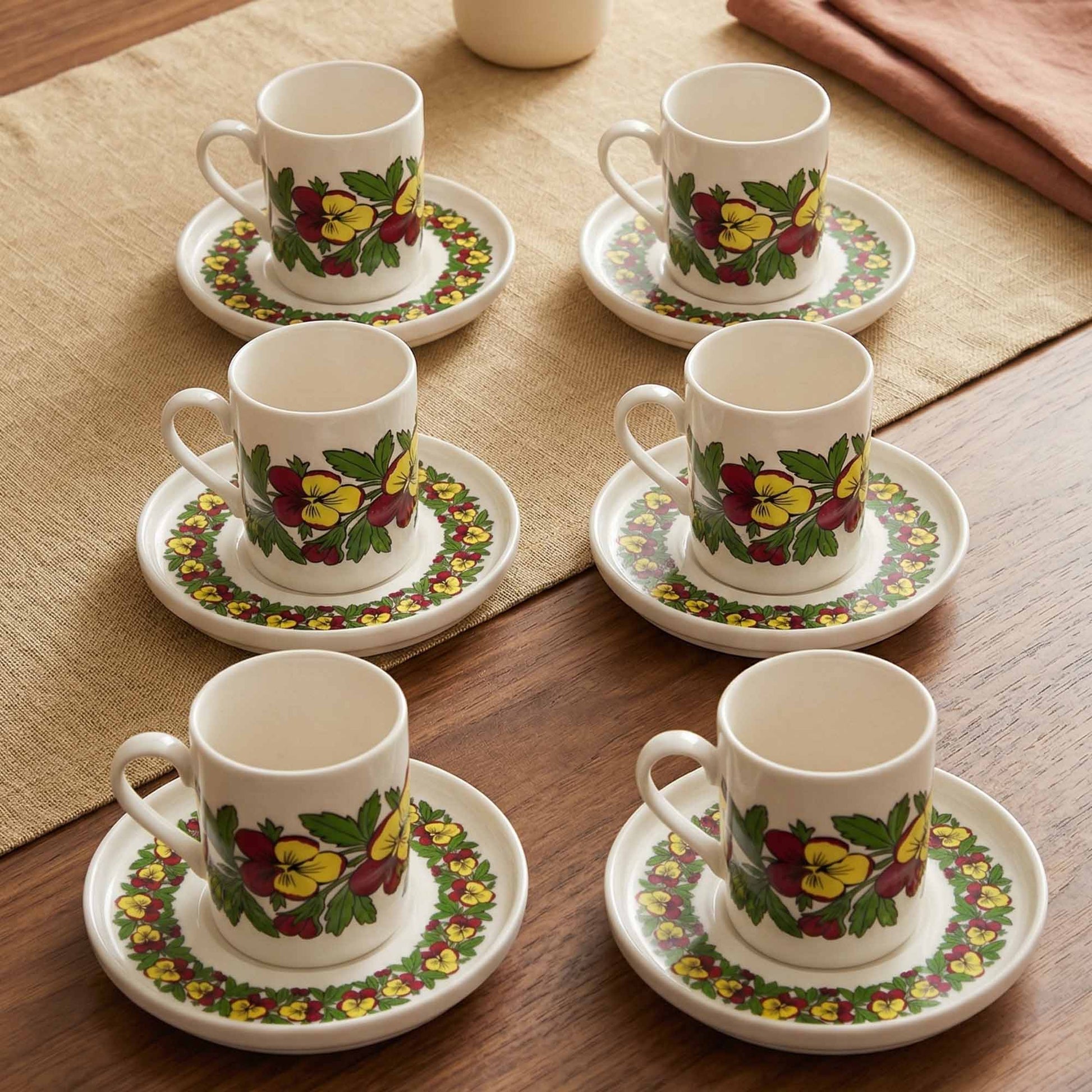 Set of six porcelain cups and saucers with floral patterns on a wooden table.