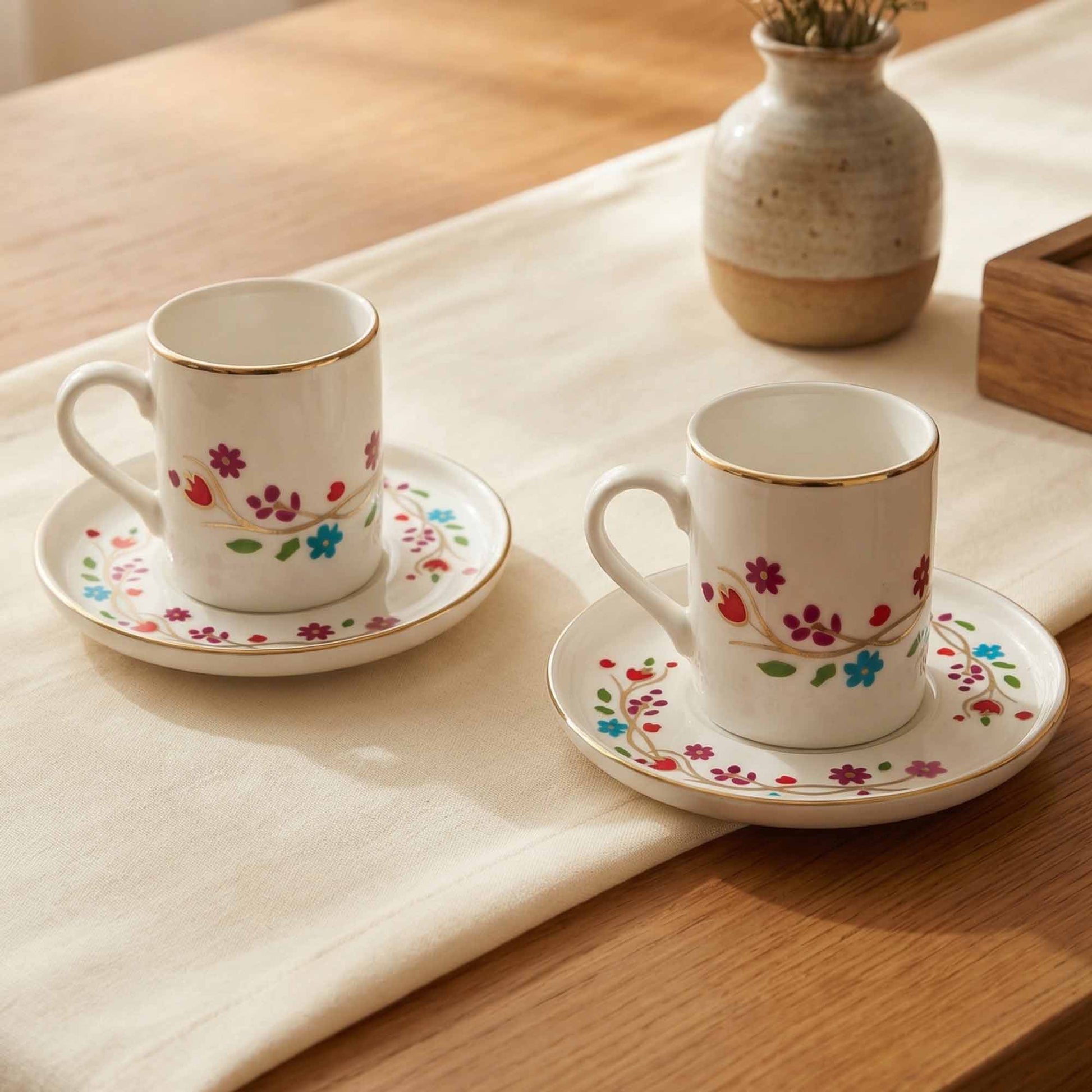 Two porcelain cups with floral designs on saucers on a wooden table.