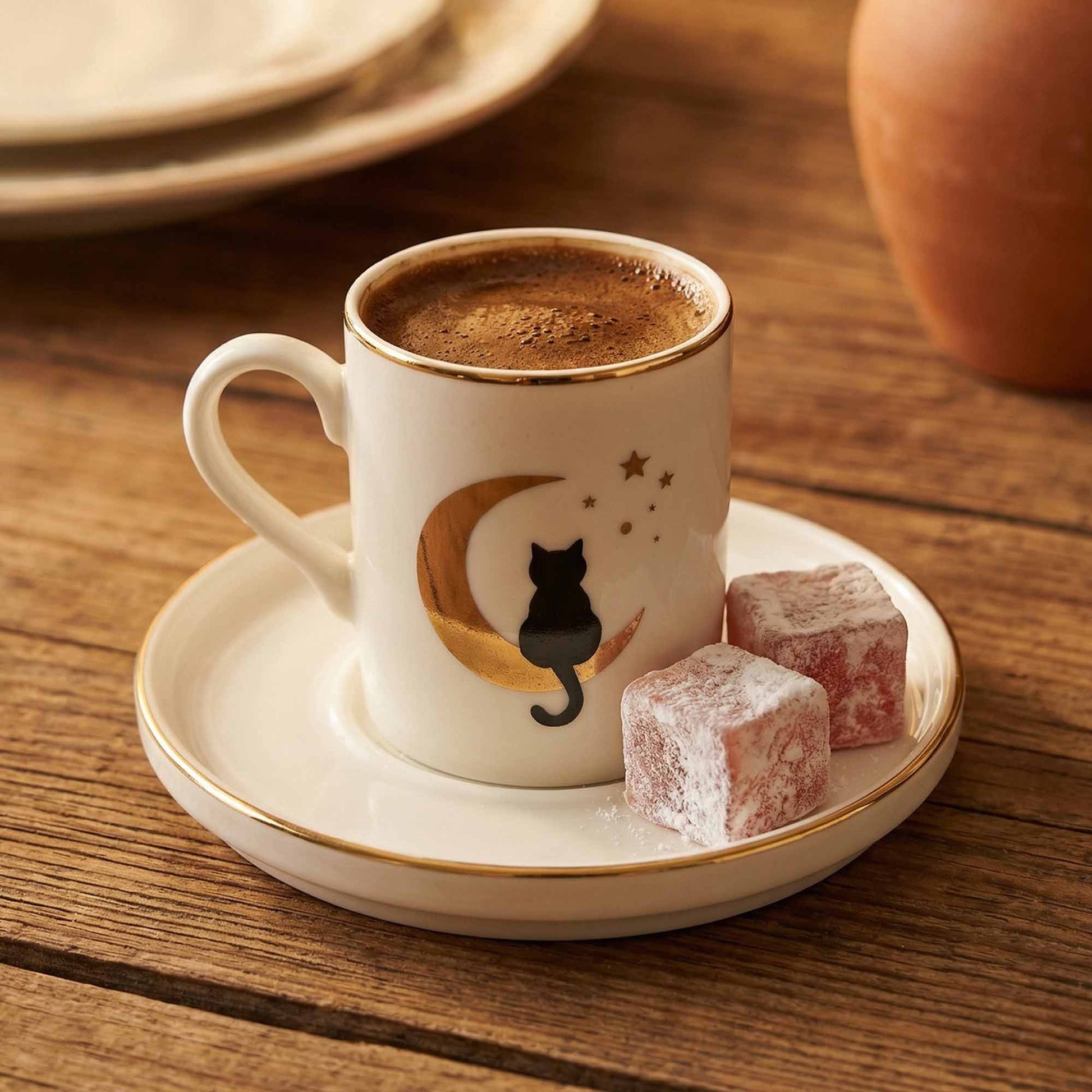 Porcelain mug with a cat design on a saucer with Turkish delight on a wooden table