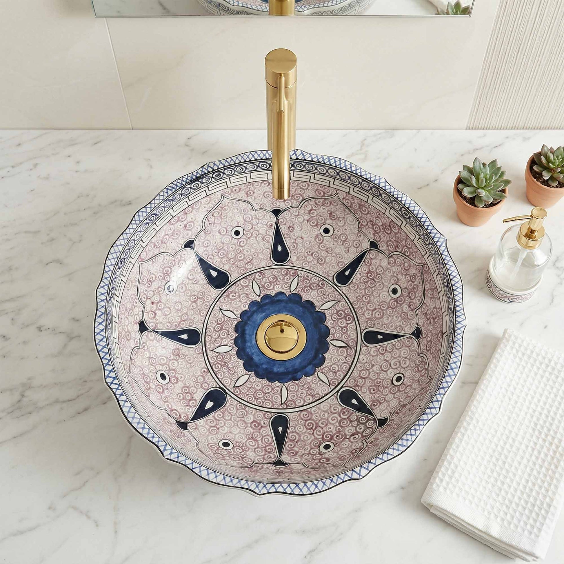 Decorative bathroom ceramic sink with artistic design and gold faucet on a marble countertop.