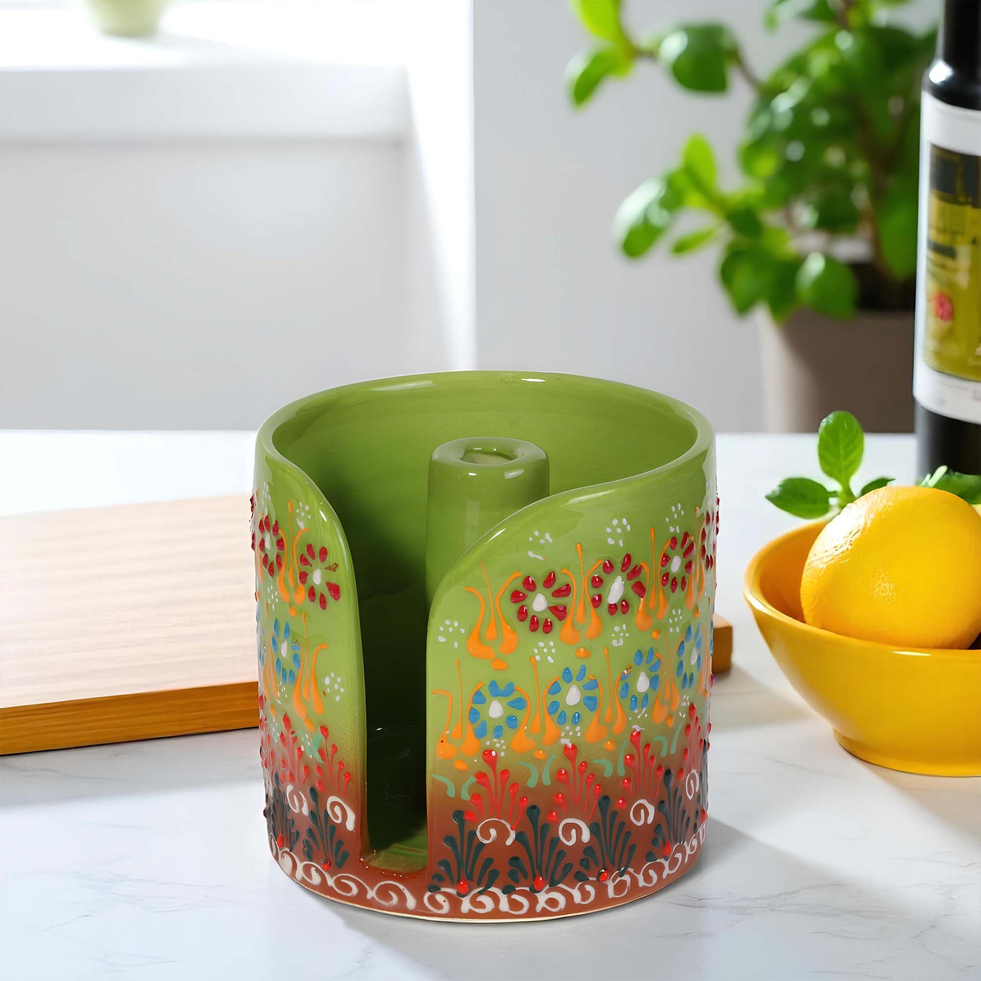 Decorative green paper towel holder with floral patterns on a table with a bowl of lemons and a book in the background.