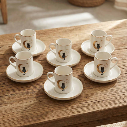 Set of six porcelain coffee cups and saucers with cat designs on a wooden table.