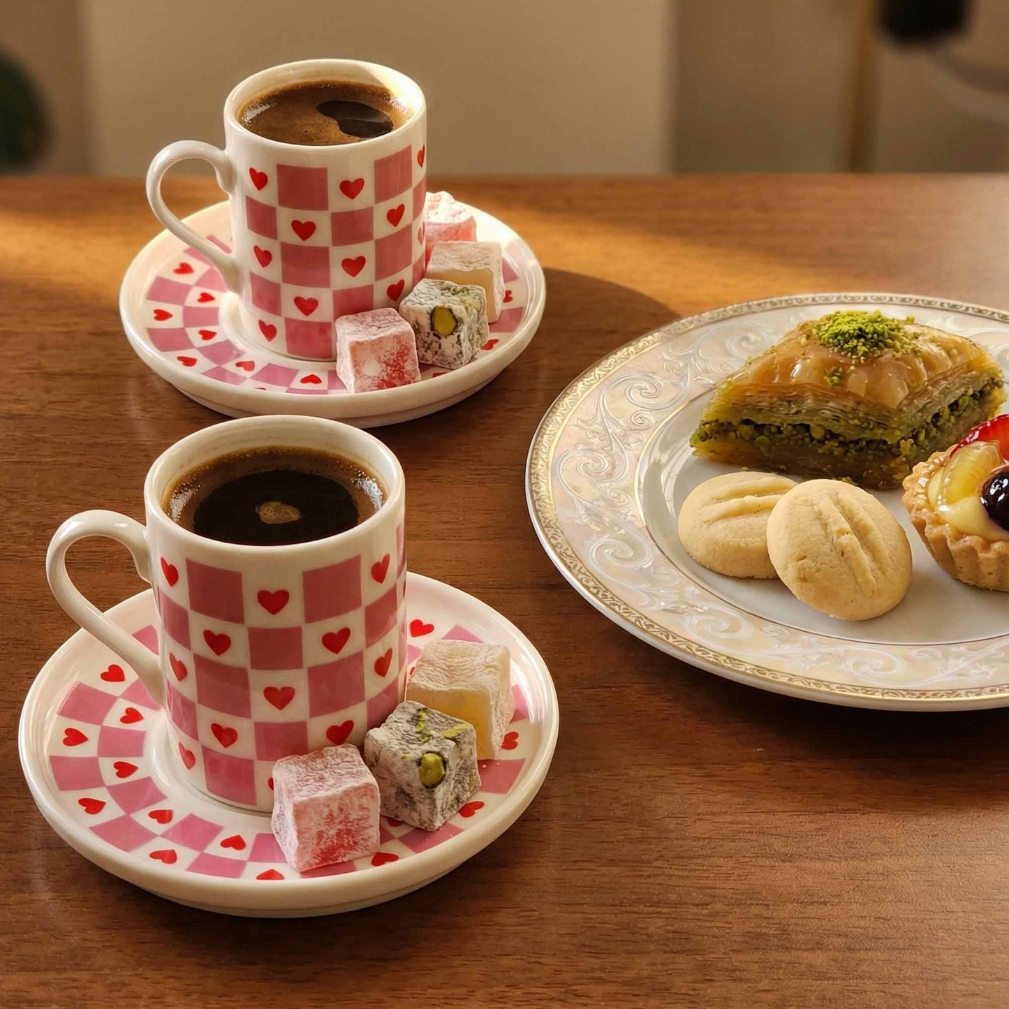 Two cups of coffee with heart patterns on saucers, accompanied by pastries and desserts on a wooden table.