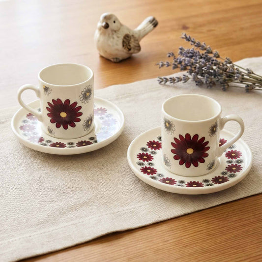 Two floral porcelain cups and saucers on a wooden table with lavender and a bird figurine.