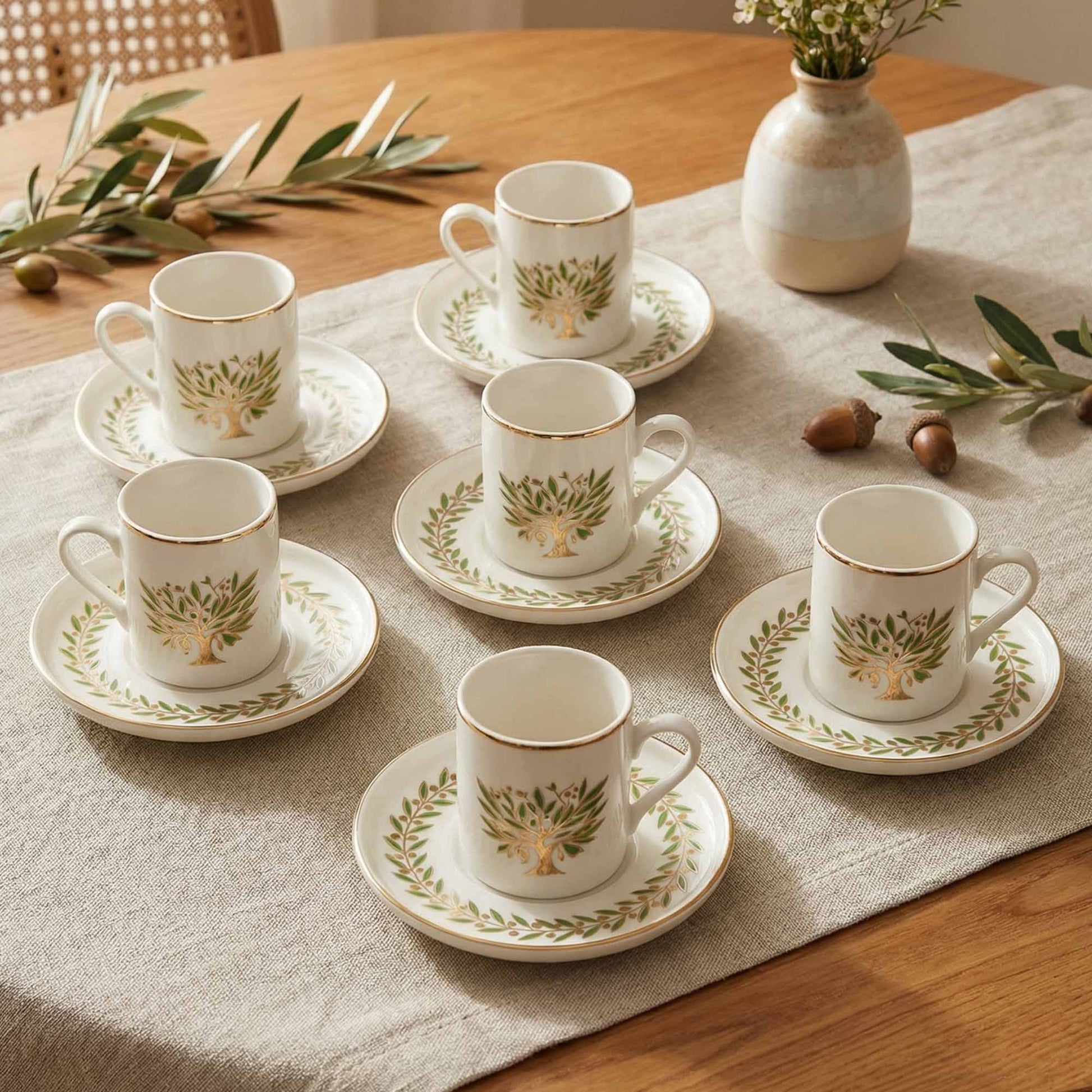 Set of white porcelain cups and saucers with green leaf patterns on a wooden table.