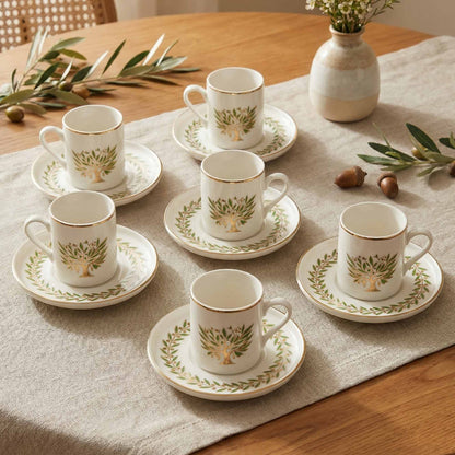 Set of white porcelain cups and saucers with green leaf patterns on a wooden table.