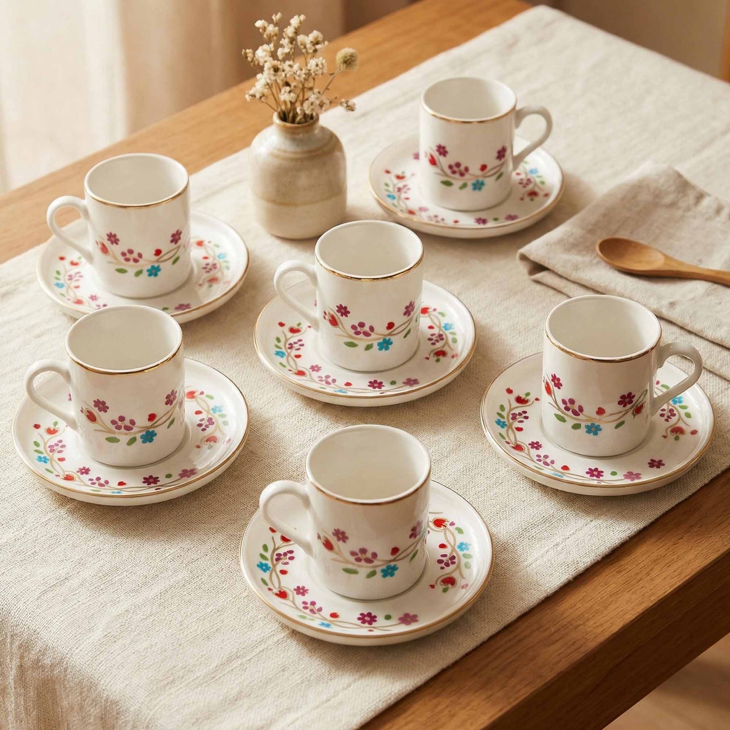 Set of floral teacups and saucers on a table with a vase and napkin.