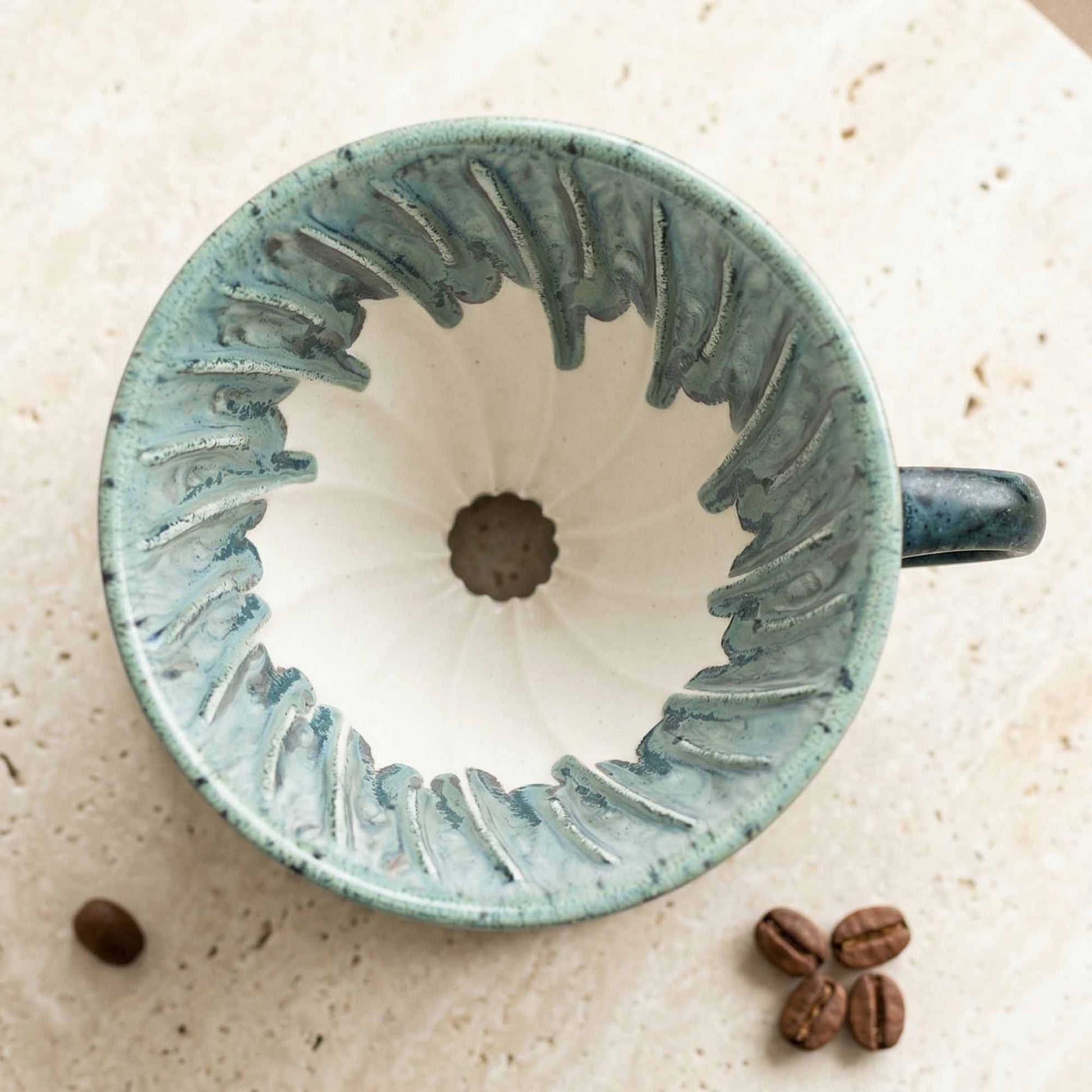 Blue ceramic coffee filter on a beige surface with coffee beans.