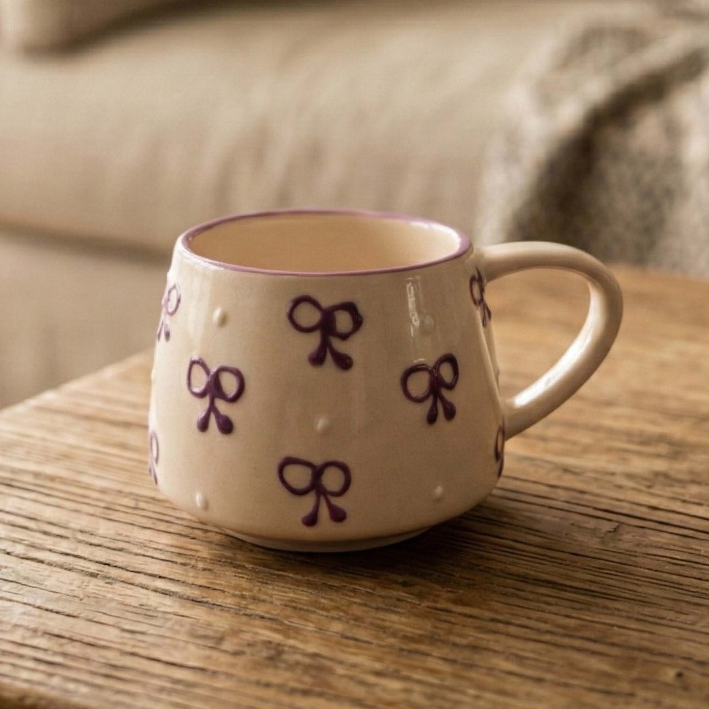 Beige mug with purple bow designs on a wooden surface