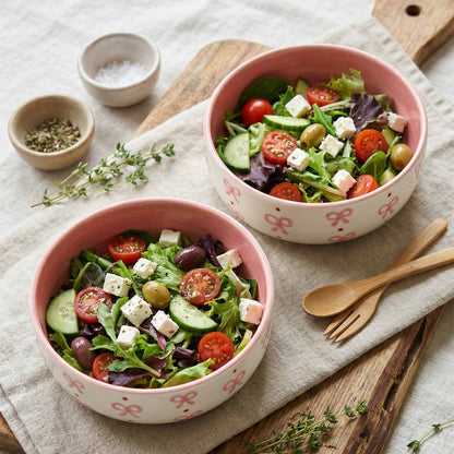 Two pink bowls filled with a salad on a wooden surface with utensils.