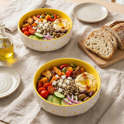 Two yellow bowls filled with a colorful salad on a table with bread and olive oil.