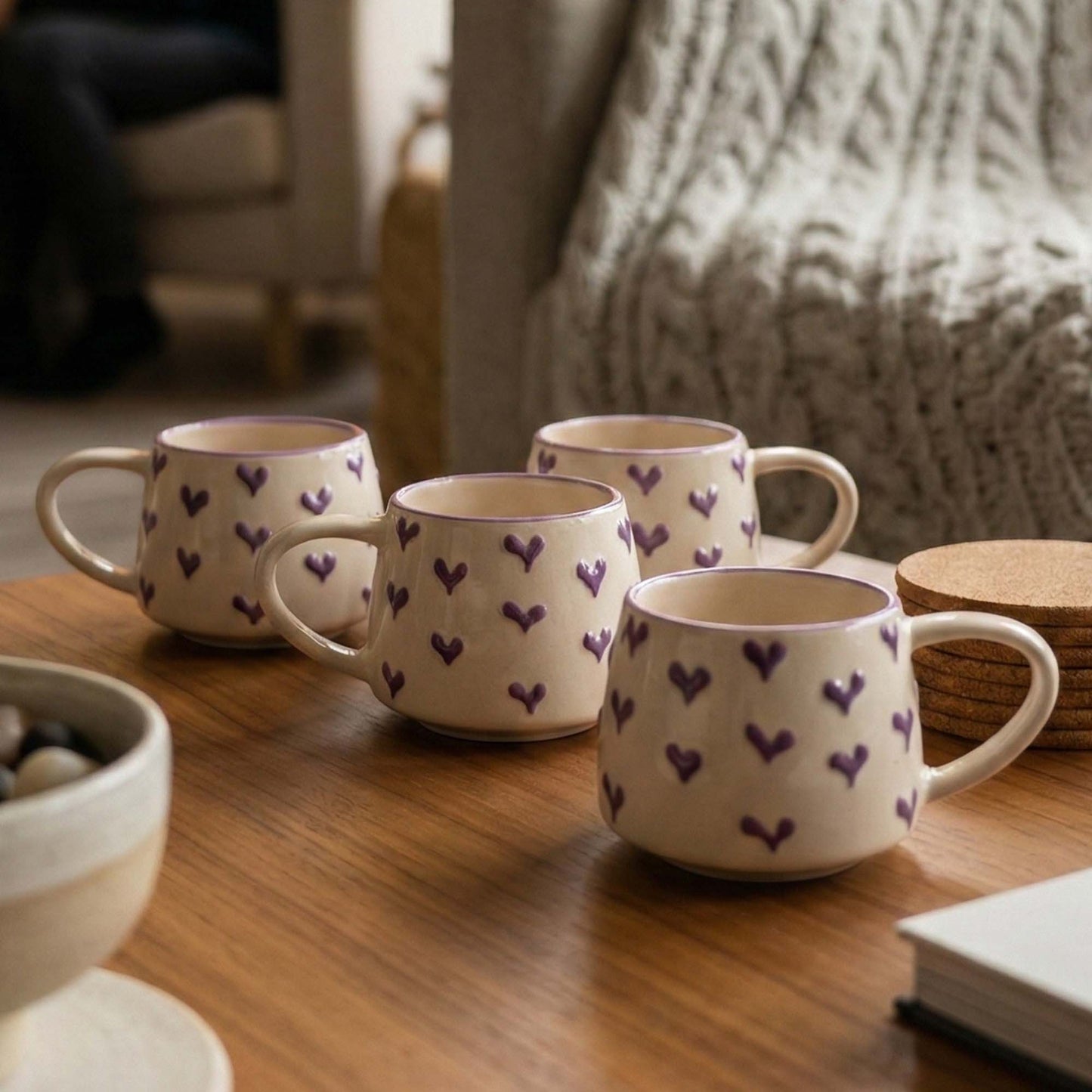 Set of four ceramic mugs with heart patterns on a wooden surface.
