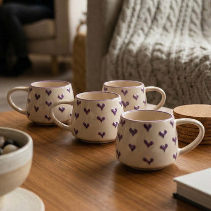 Set of four ceramic mugs with heart patterns on a wooden surface.