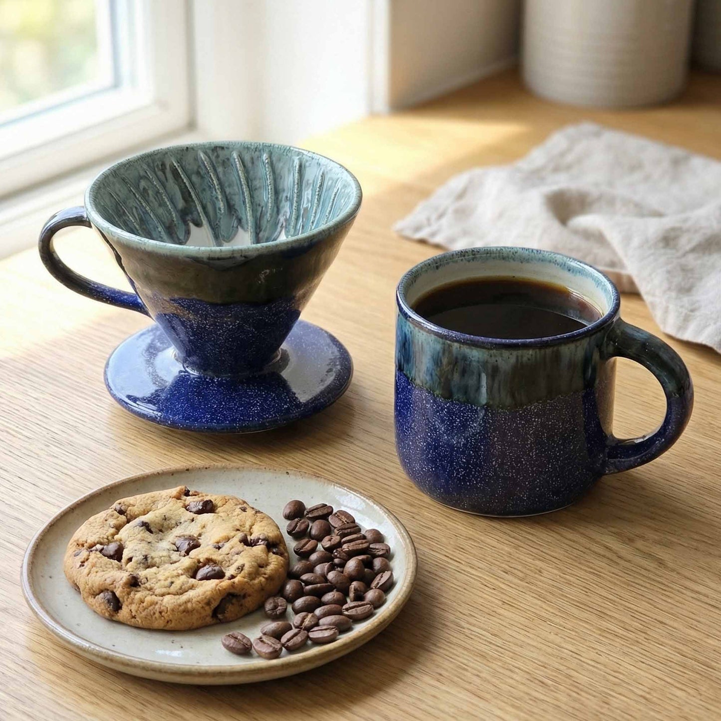 Two blue ceramic mugs with a plate of cookies and coffee beans on a wooden table.