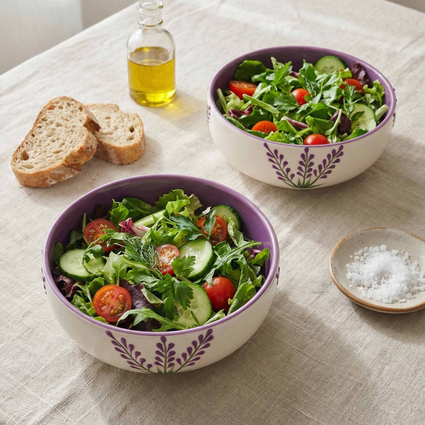 Two bowls of salad with bread and oil on a tablecloth