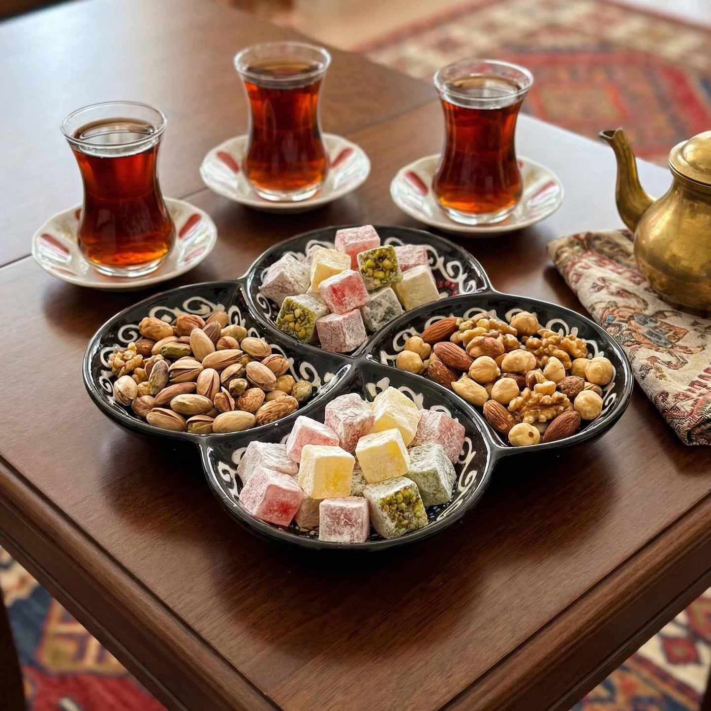 Assorted Turkish delight and nuts on a decorative tray with three glasses of tea on a wooden table.
