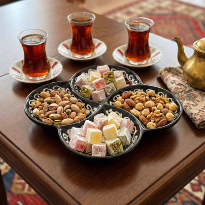 Assorted Turkish delight and nuts on a decorative tray with three glasses of tea on a wooden table.