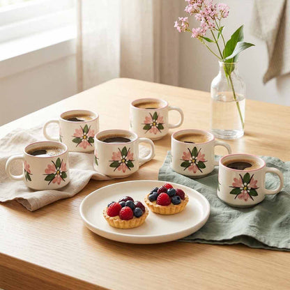 Set of floral mugs with coffee and pastries on a wooden table.