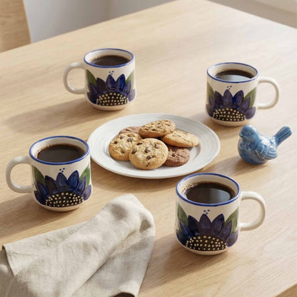 Four ceramic mugs with floral designs filled with coffee, a plate of cookies on a wooden table.