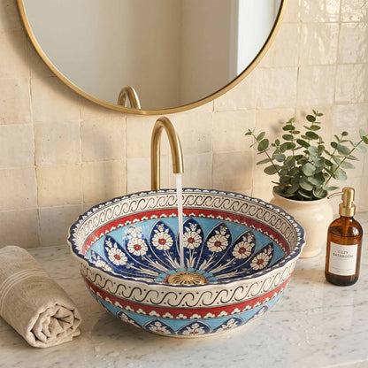 Decorative bathroom sink with floral patterns, gold faucet, and plant in the background.