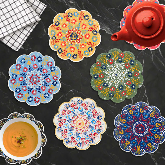 Colorful floral trivets on a dark surface with a red teapot and checkered cloth.