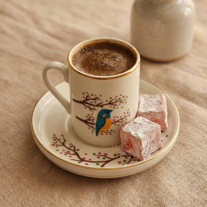 Cup of coffee with a decorative saucer and two pieces of Turkish delight on a beige surface.