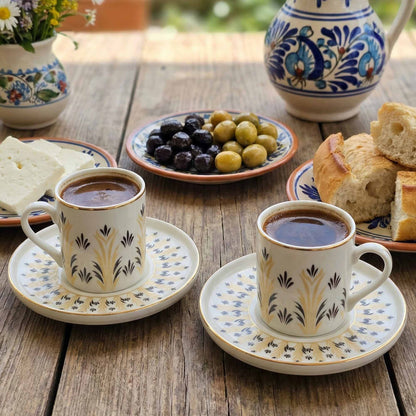 Two cups of coffee with saucers on a wooden table with snacks and a decorative teapot.