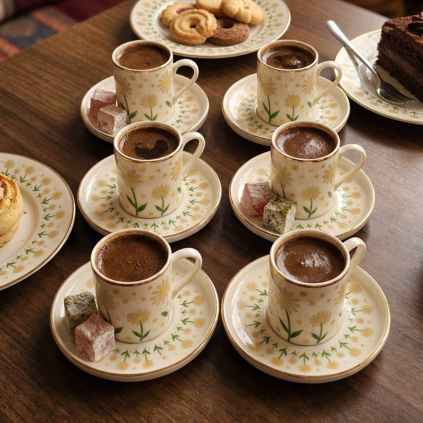 Set of coffee cups with floral patterns on a wooden table with pastries.