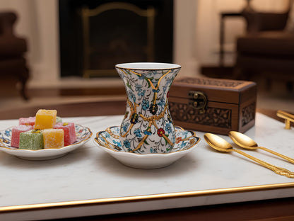 Decorative teacup with floral patterns on a marble surface with pastries and spoons.