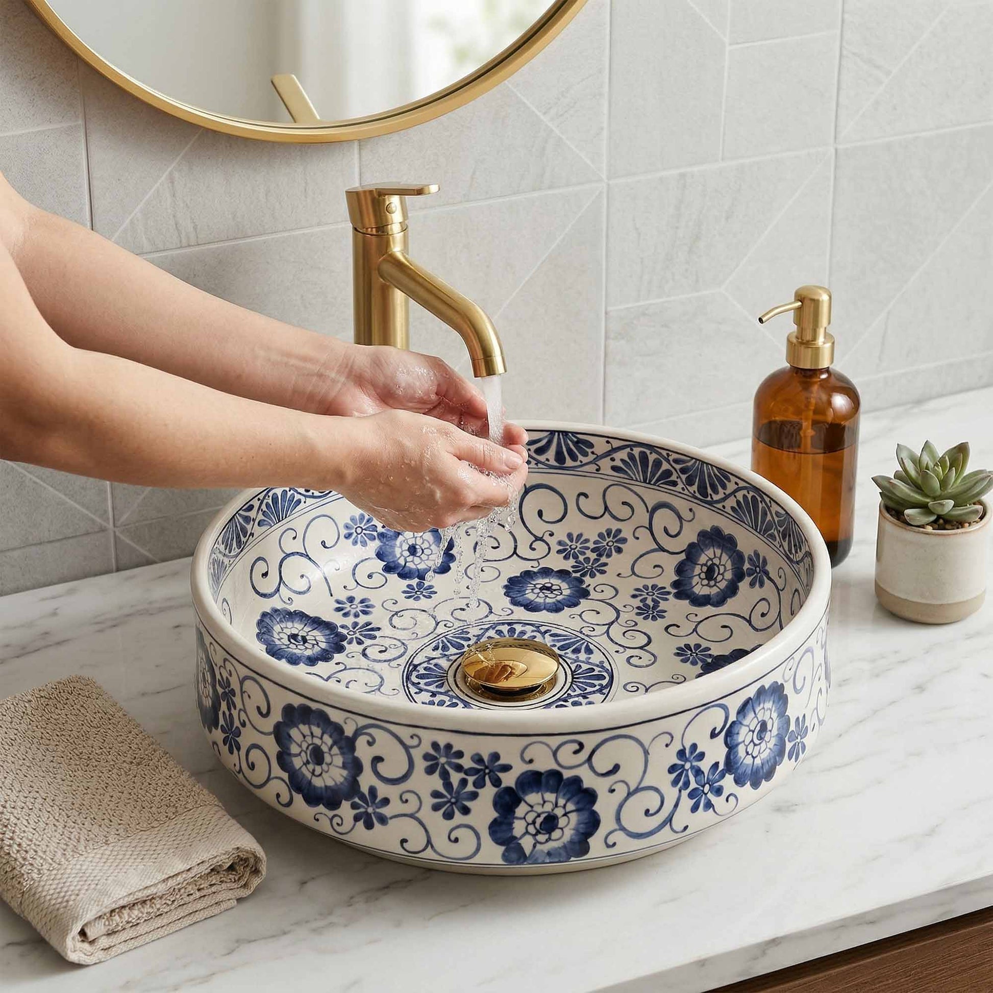 Person washing hands under a gold faucet in a bathroom with a decorative blue and white sink.