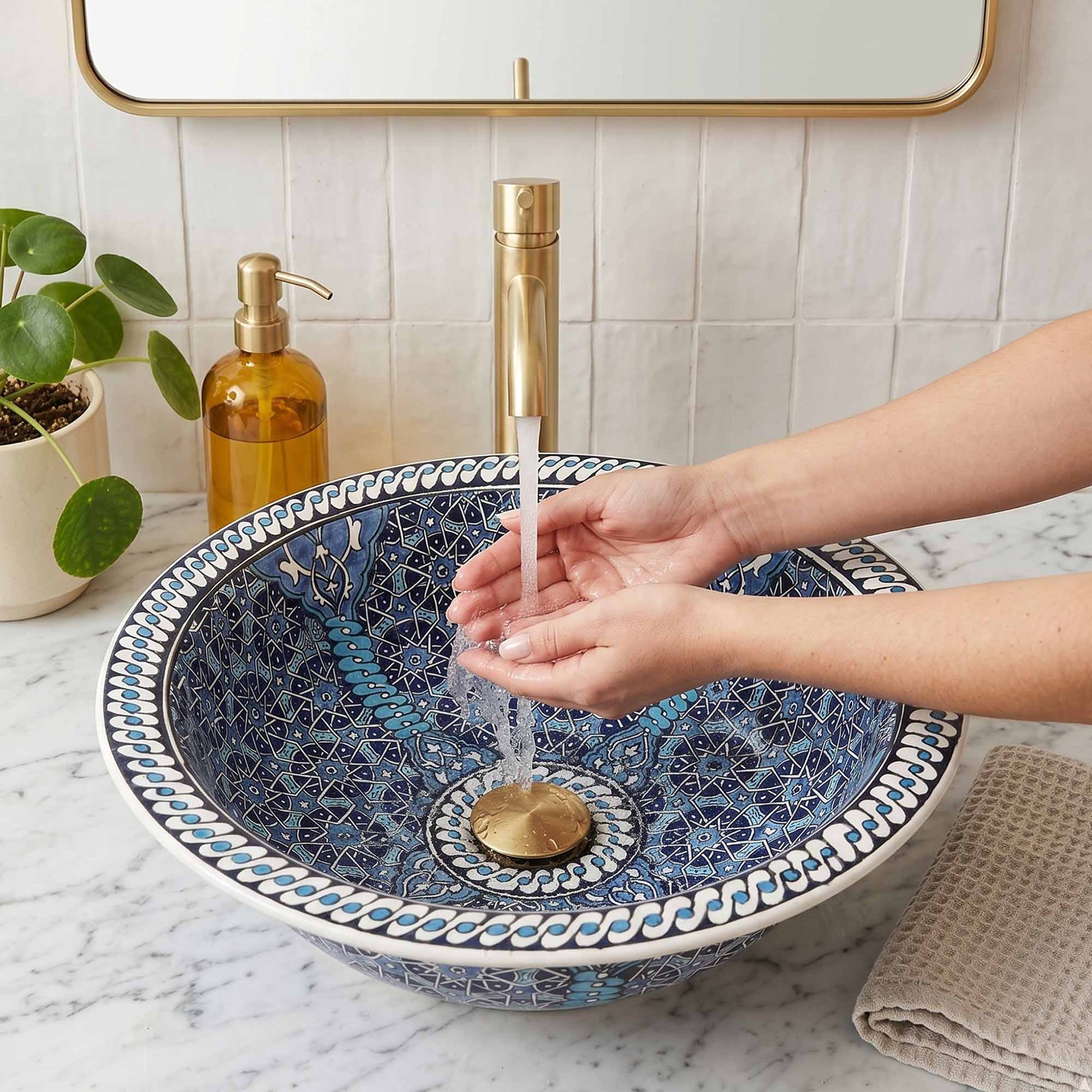 Person washing hands under a blue mosaic sink with gold fixtures.