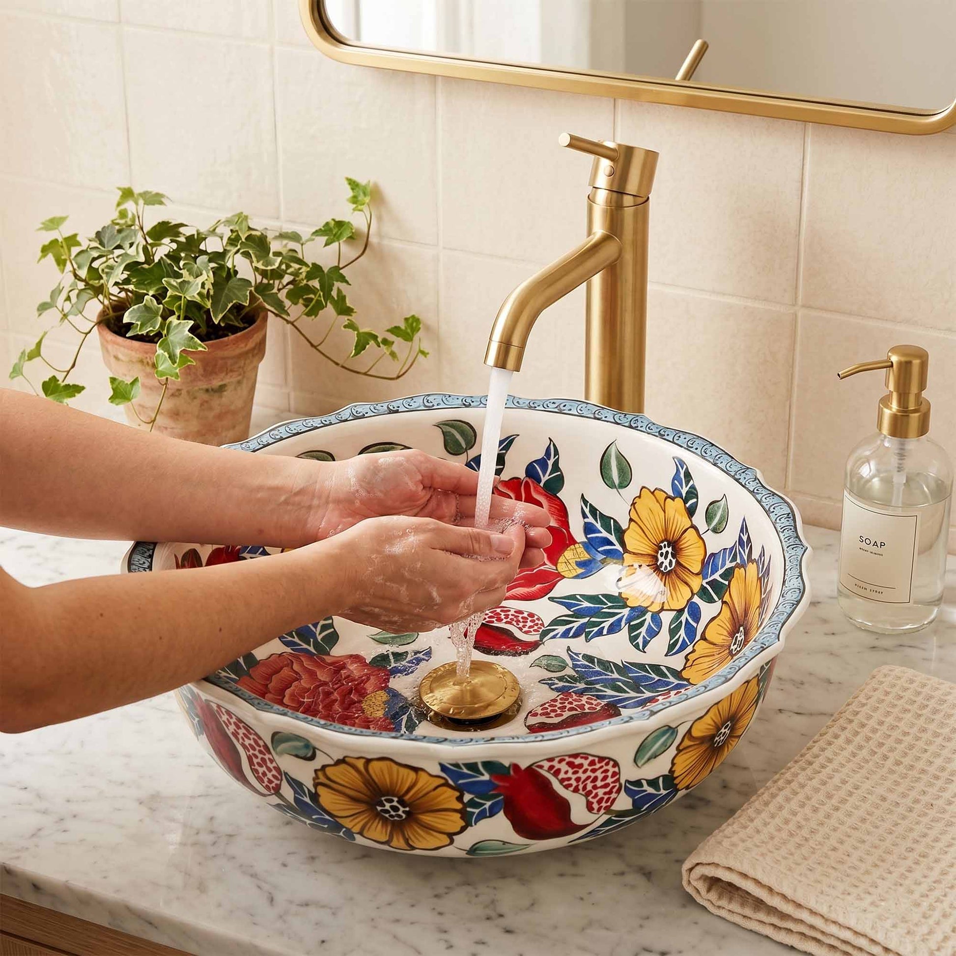 Person washing hands under a colorful floral sink with a gold faucet.